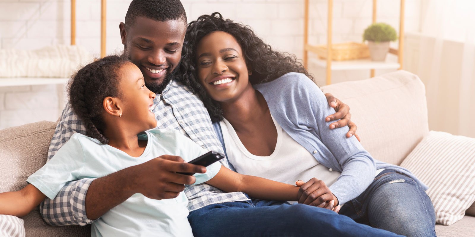 smiling African American man and woman snuggling on couch with child